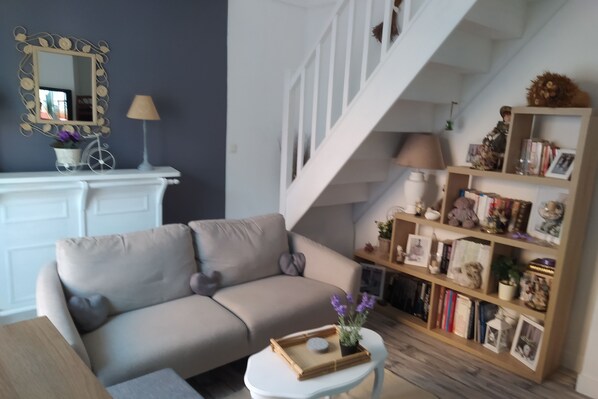 A living room with a beige sofa, a small white table with a tray, a bookshelf, and a staircase.