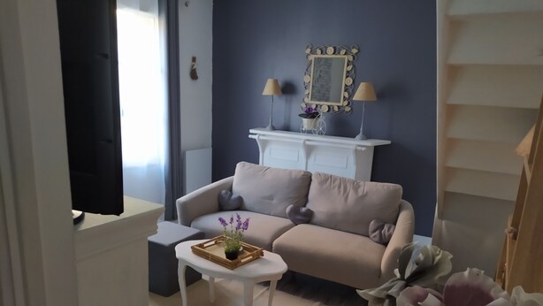 Un salon avec un canapé beige, une table basse blanche ornée d’un plateau de fleurs, une table d’appoint blanche et un miroir décoratif sur un mur bleu foncé.