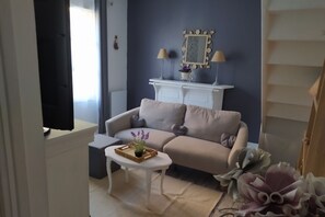 A living room with a beige sofa, a white coffee table with a tray of flowers, a white side table, and a decorative mirror on a dark blue wall.
