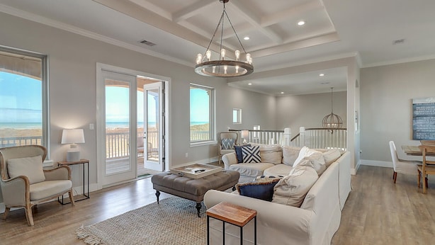 A spacious living room with a large sectional sofa, a wooden coffee table, and a chandelier. - Secluded beachfront subdivision with a boardwalk to the beach, private pool! (Port Aransas)