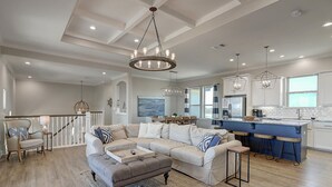 A spacious living room with a large beige sectional sofa, a wooden coffee table, and a chandelier. - Secluded beachfront subdivision with a boardwalk to the beach, private pool! (Port Aransas)