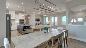 A spacious kitchen with a central island, modern lighting fixtures, and a view of the ocean through large windows. - Secluded beachfront subdivision with a boardwalk to the beach, private pool! (Port Aransas)