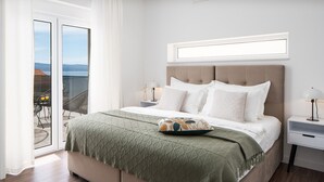 A bedroom with a bed, a nightstand, a window with a view, and a balcony with chairs and a table.