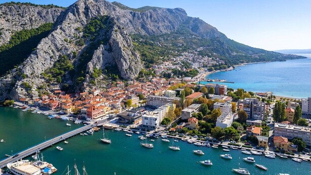 A coastal town with a marina, buildings, and mountainous backdrop.