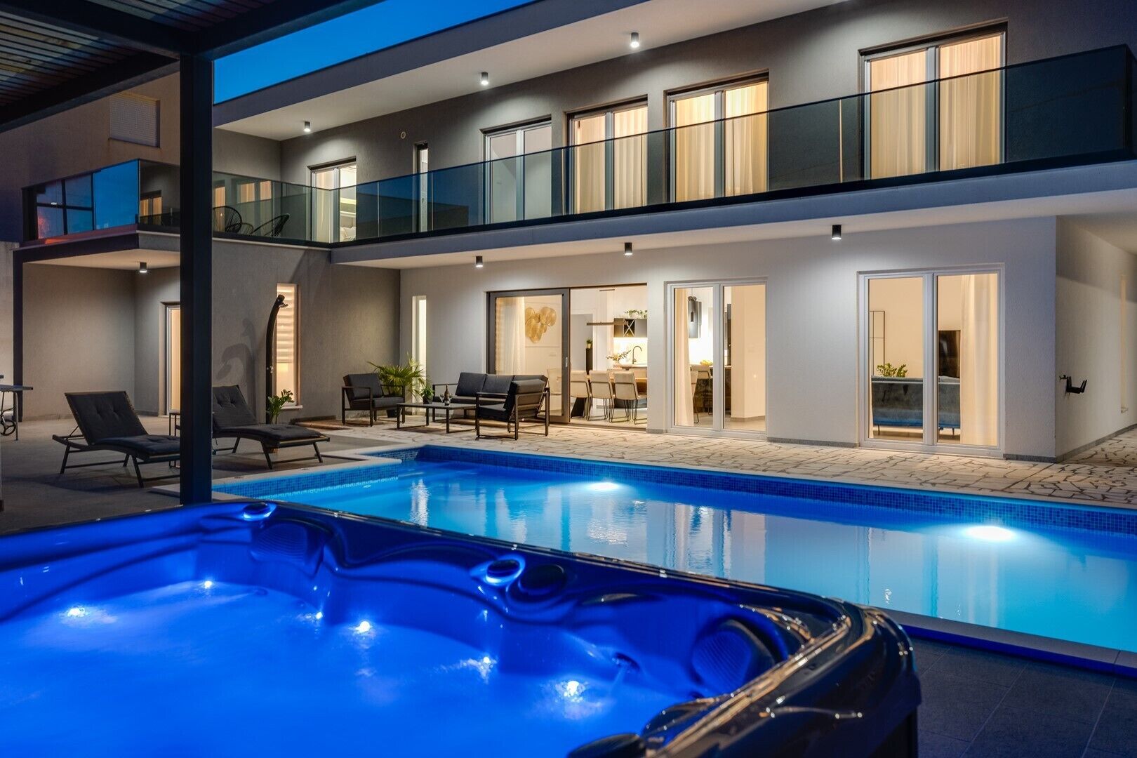 Une maison moderne à deux étages dotée d’une piscine, d’un espace salon extérieur et d’un jacuzzi.