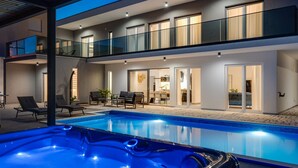 A modern two-story house with a swimming pool, outdoor seating, and a hot tub.