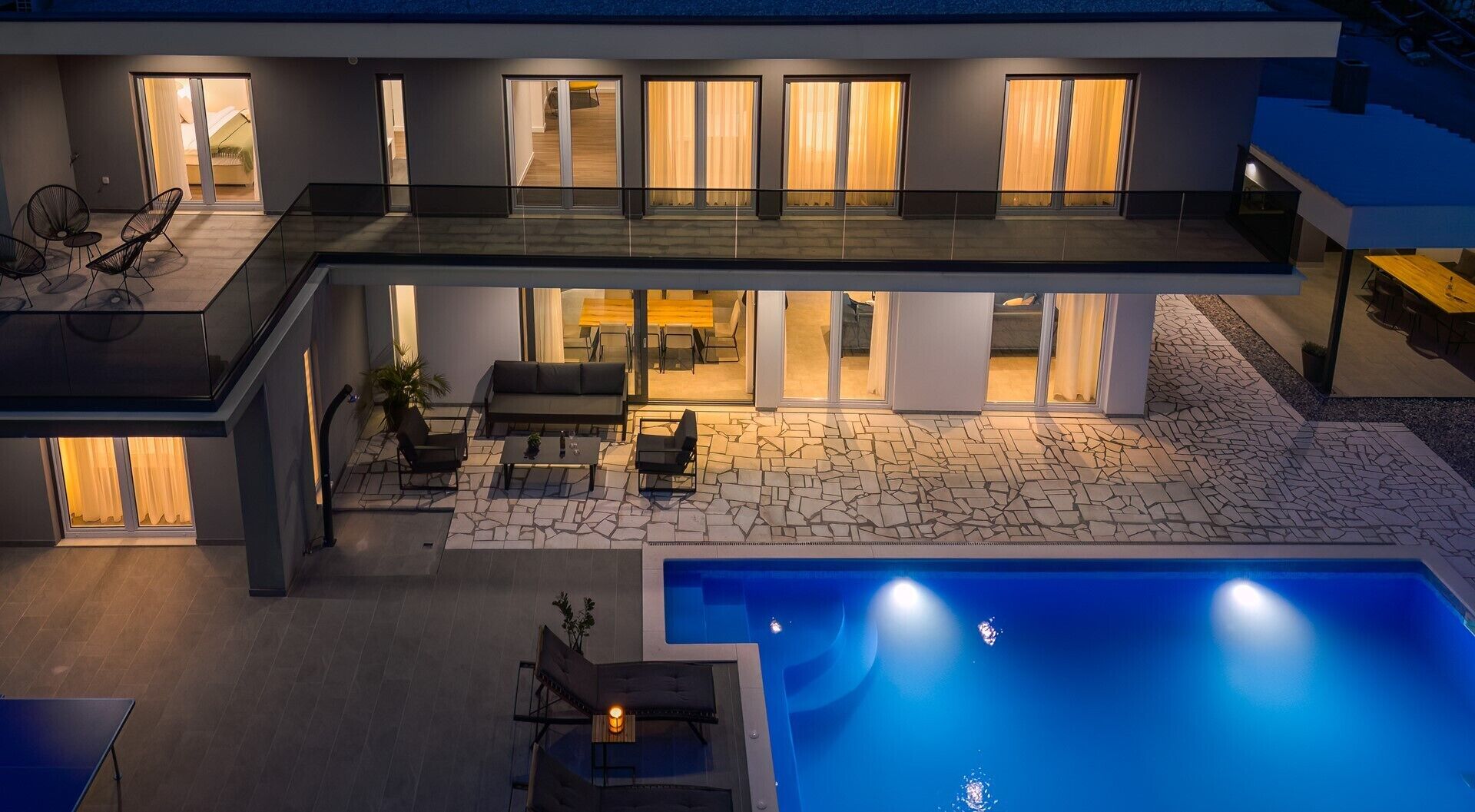 A modern two-story house with a swimming pool, outdoor seating, and large windows.