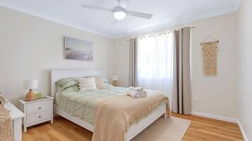 A bedroom with a bed, nightstands, a ceiling fan, a window with curtains, and a macrame wall hanging.