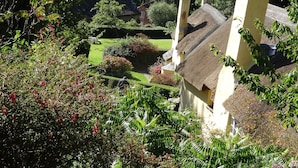 A traditional building with a thatched roof, surrounded by lush greenery and a view of rolling hills.