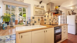 A kitchen with a sink, stove, and refrigerator. There are decorative items on the counter and a window with a view of greenery.