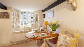 A dining area with a table set for two, a window with curtains, a radiator, and a mounted deer head on the wall.
