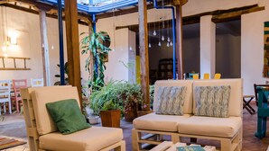 Un espacio interior acogedor con dos sillones cómodos y una mesita baja, rodeado de plantas en macetas y lámparas colgantes.
