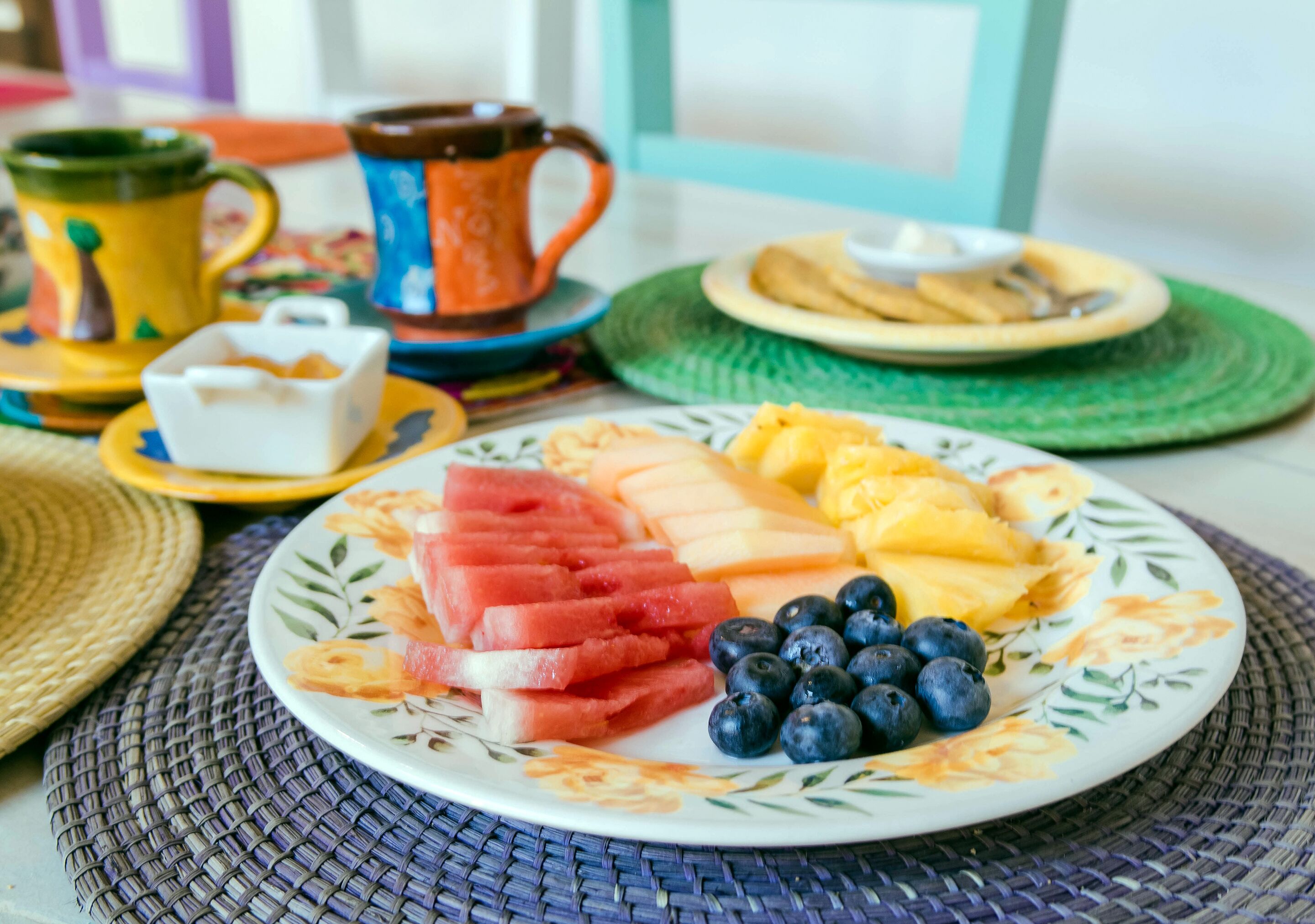 A plate of watermelon, pineapple, and blueberries on a table with a woven placemat.