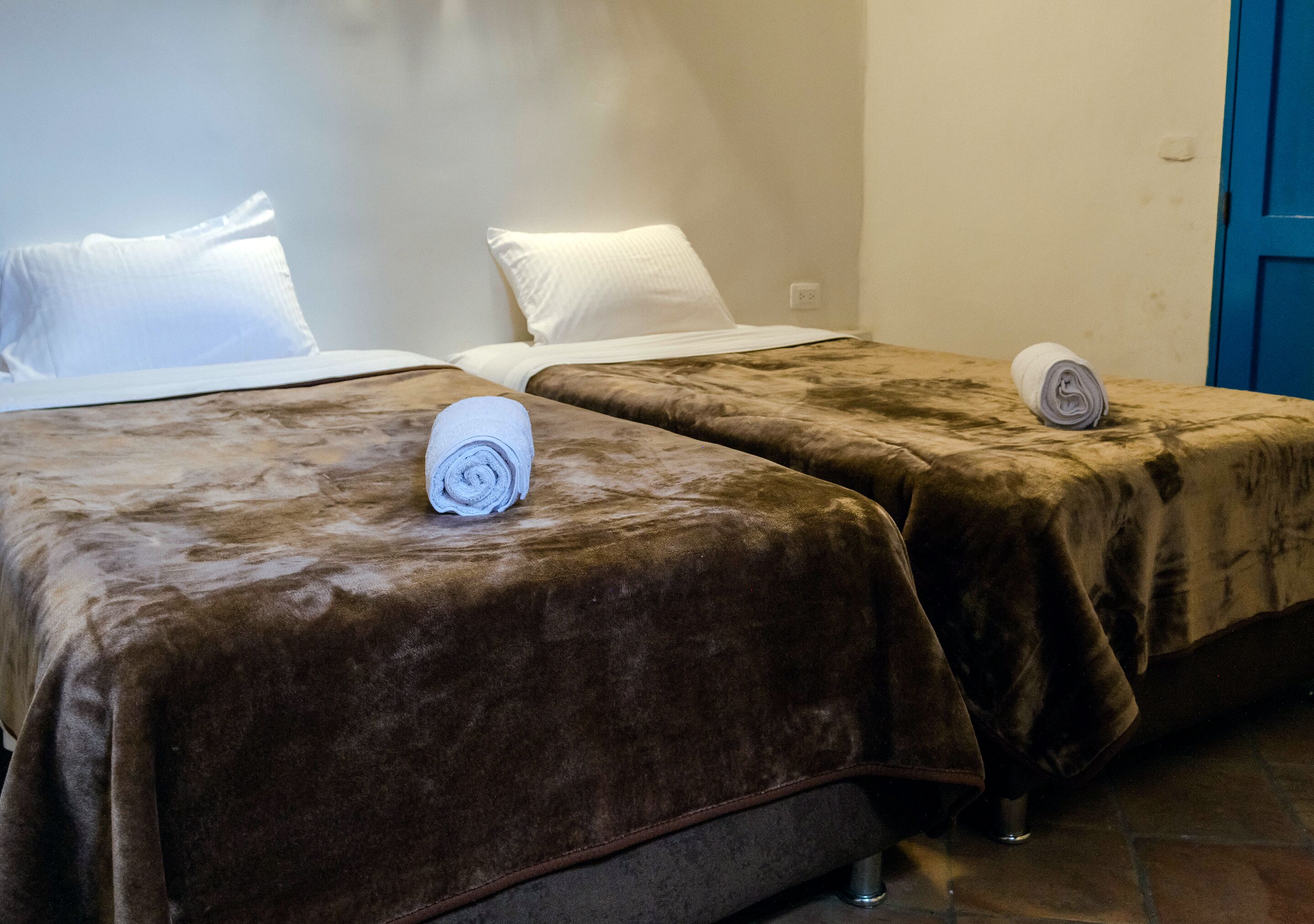 Twee bedden met bruine dekens, witte kussens en opgerolde handdoeken.