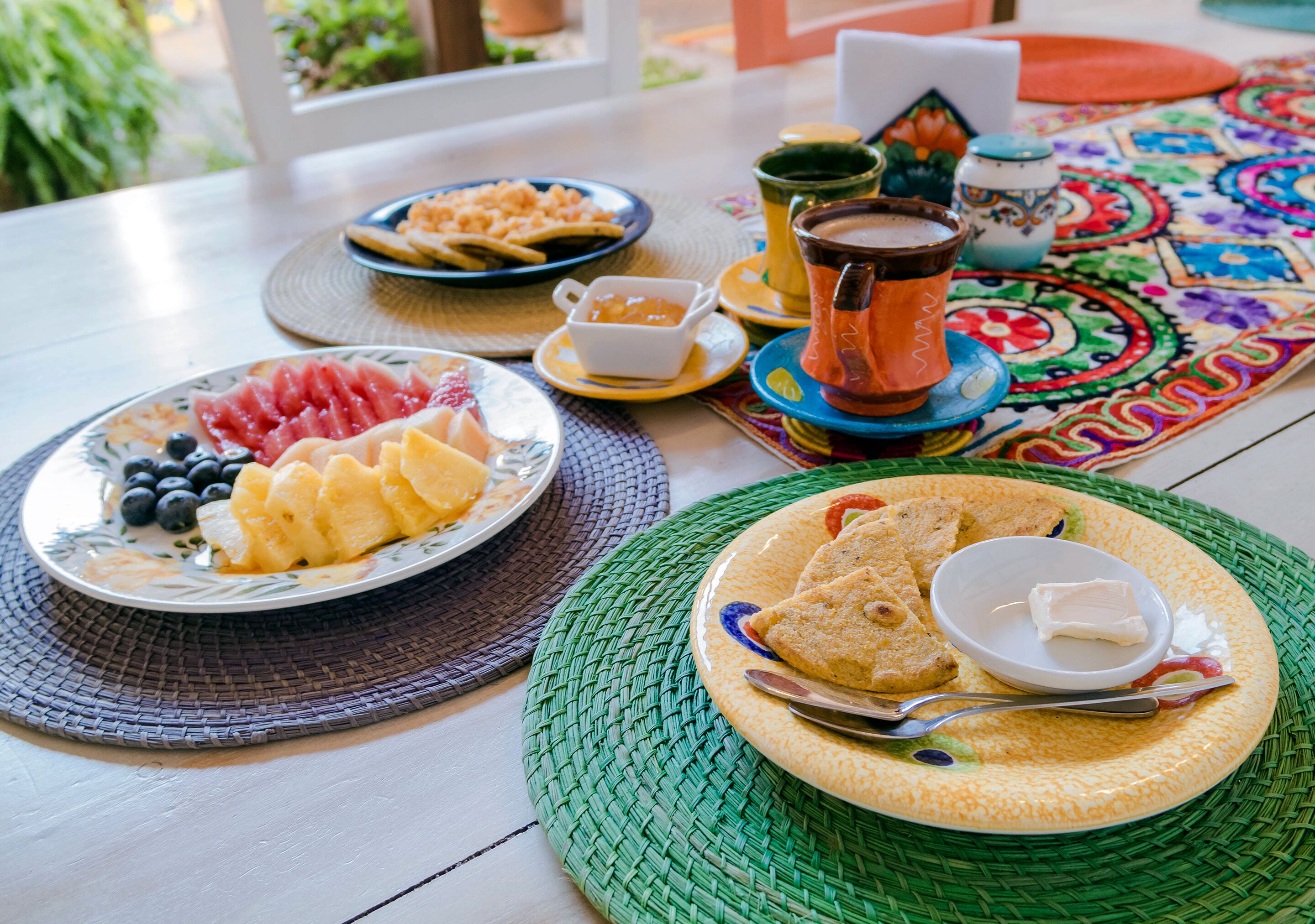 Une table de petit-déjeuner avec des assiettes de fruits, du pain et une tasse de café.