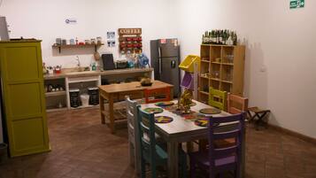 Cocina compacta con comedor, equipada con refrigerador, estación de café y repisas con botellas y vasos.
