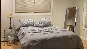 Quarto com cama, mesa de cabeceira, luminária, espelho e janela com persianas.
