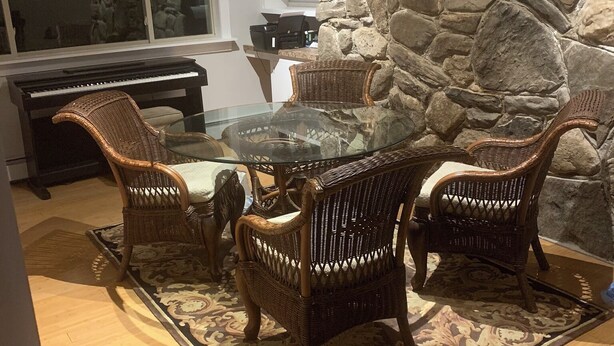 Uma sala de estar aconchegante com parede de pedra, um piano, cadeiras de vime e uma mesa de vidro.