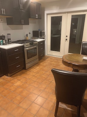 Een keuken met donkere kastjes, een fornuis, oven en een magnetron. Er staat een eettafel met een stoel.
