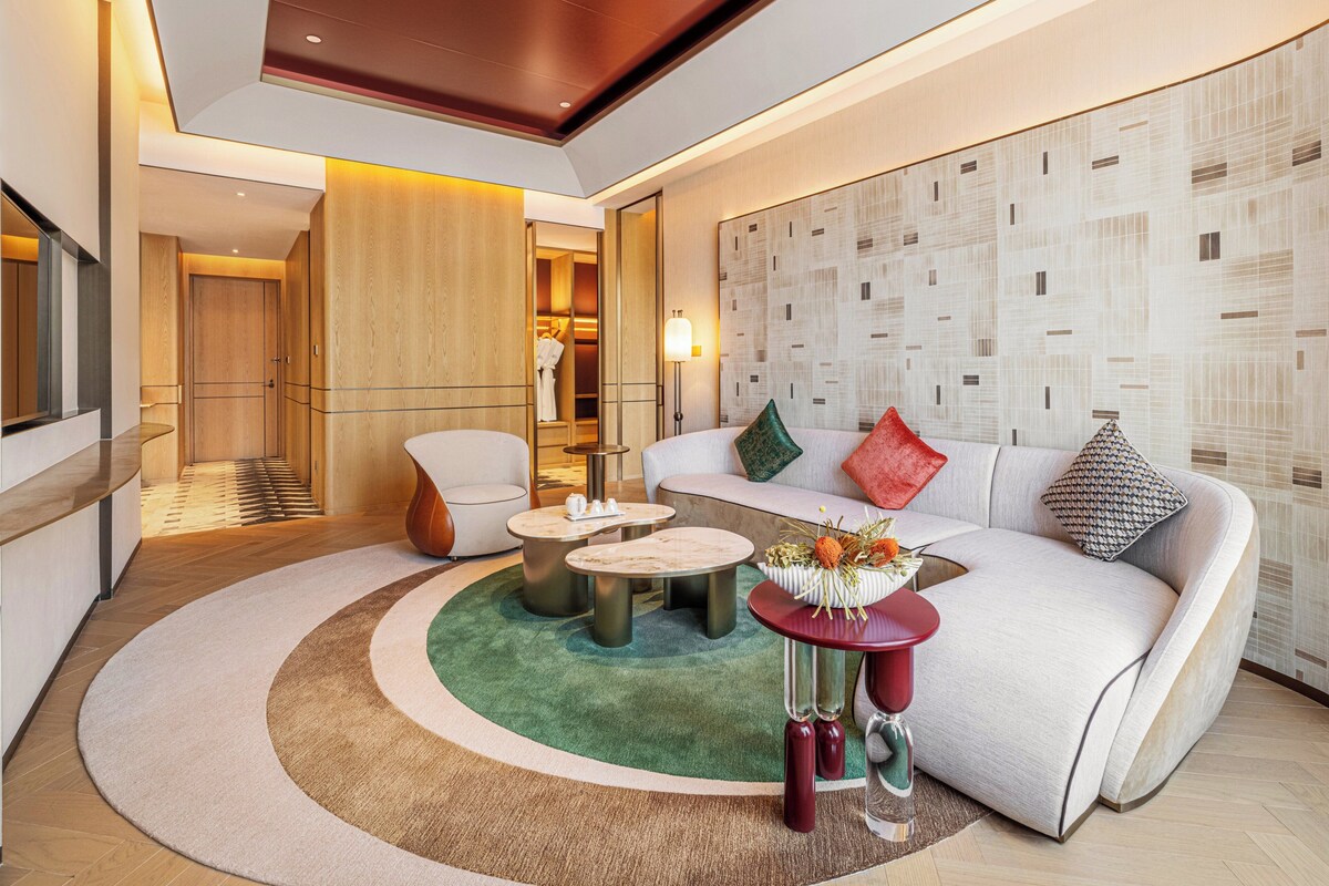 A modern hotel room with a curved sofa, a round coffee table, and a seating area with a patterned wall.