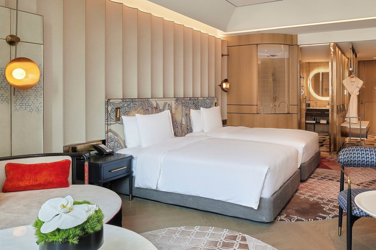A modern hotel room with a large bed, bedside tables, a desk, and a seating area with a chair and table.