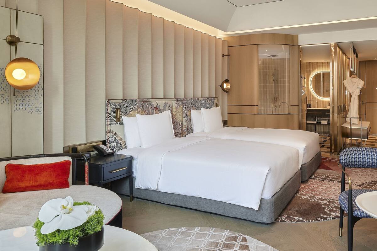 A modern hotel room with a large bed, bedside tables, a desk, and a seating area with a chair and table.