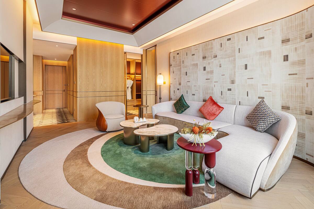 A modern hotel room with a curved sofa, a round coffee table, and a seating area with a patterned wall.