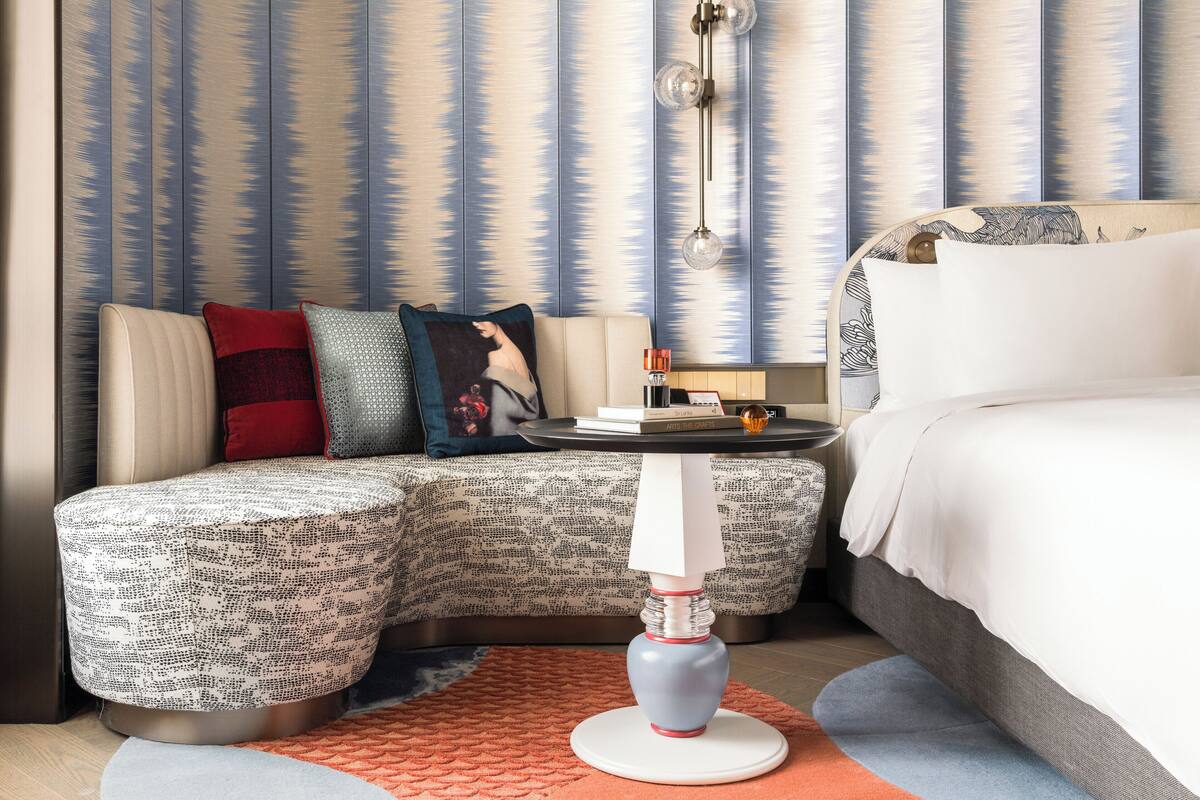 A modern hotel room with a sofa, a bedside table, a lamp, and a bed.