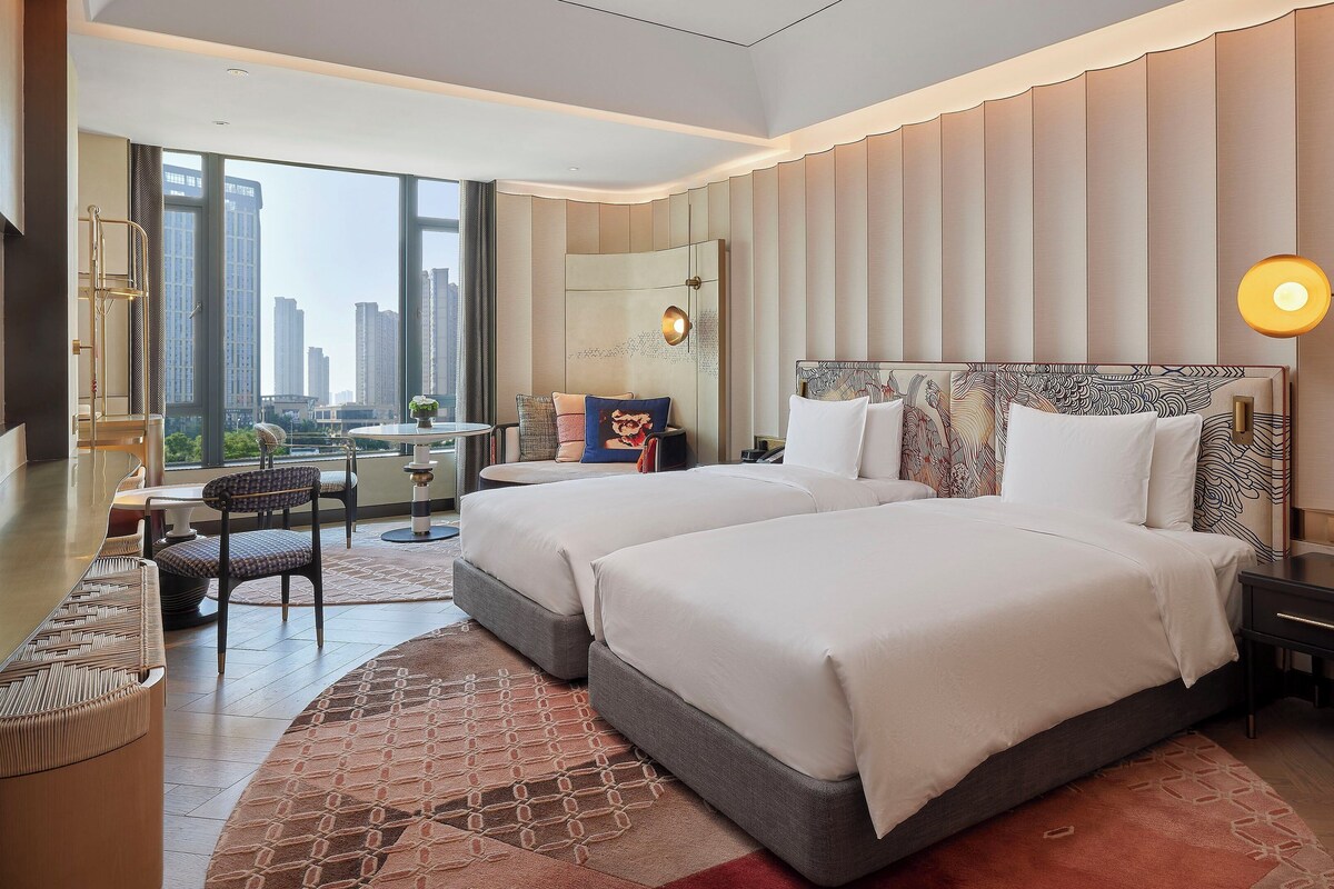 A modern hotel room with a large bed, a desk, and a view of the city.
