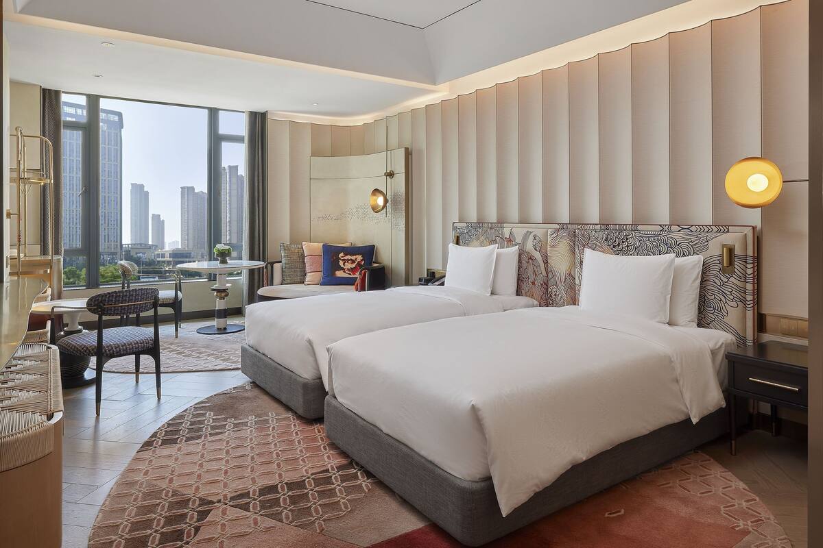 A modern hotel room with a large bed, a desk, and a view of the city.