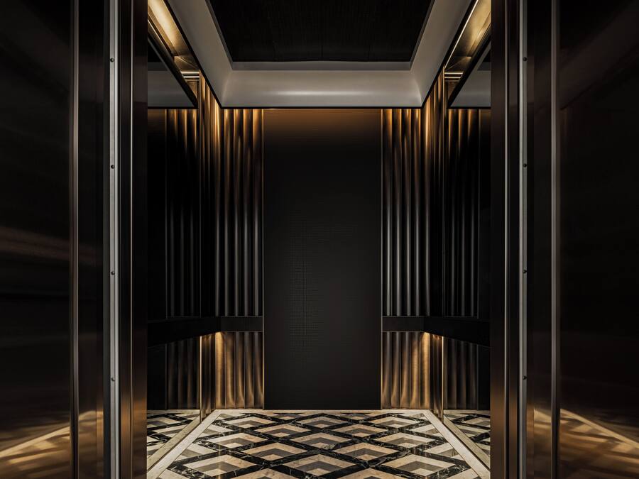 Interno di un ascensore con pareti metalliche, pavimento a disegno e luce al soffitto.
