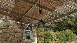 An outdoor patio with a glass-top table and white metal chairs, surrounded by stone walls and a thatched roof. - House La Luberonne Gordes Vaucluse Provence. Heated pool from May 15. (Gordes)