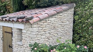 A stone building with a tiled roof, a wooden door, and a garden with blooming roses. - House La Luberonne Gordes Vaucluse Provence. Heated pool from May 15. (Gordes)
