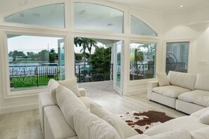 A spacious living room with a large arched glass door leading to a balcony, white sofas, and a view of a body of water. - 8500sf Intracoastal Mansion/Cinema/Dock/Pool (Hollywood)