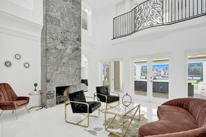A spacious living area with a high ceiling, a large stone pillar, and a balcony with a wrought iron railing. - 8500sf Intracoastal Mansion/Cinema/Dock/Pool (Hollywood)