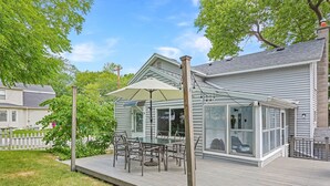 Eine überdachte Terrasse mit Tisch und Stühlen, einem großen Sonnenschirm und Blick auf ein Haus.