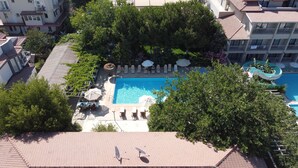 An aerial view of a hotel with a swimming pool surrounded by lounge chairs and umbrellas, a children's play area, and lush greenery. - Pasha Hotel (Fethiye)