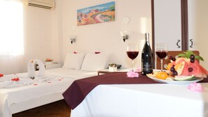 A hotel room with two beds, a painting on the wall, a bottle of wine, and a fruit plate on the nightstand. - Pasha Hotel (Fethiye)