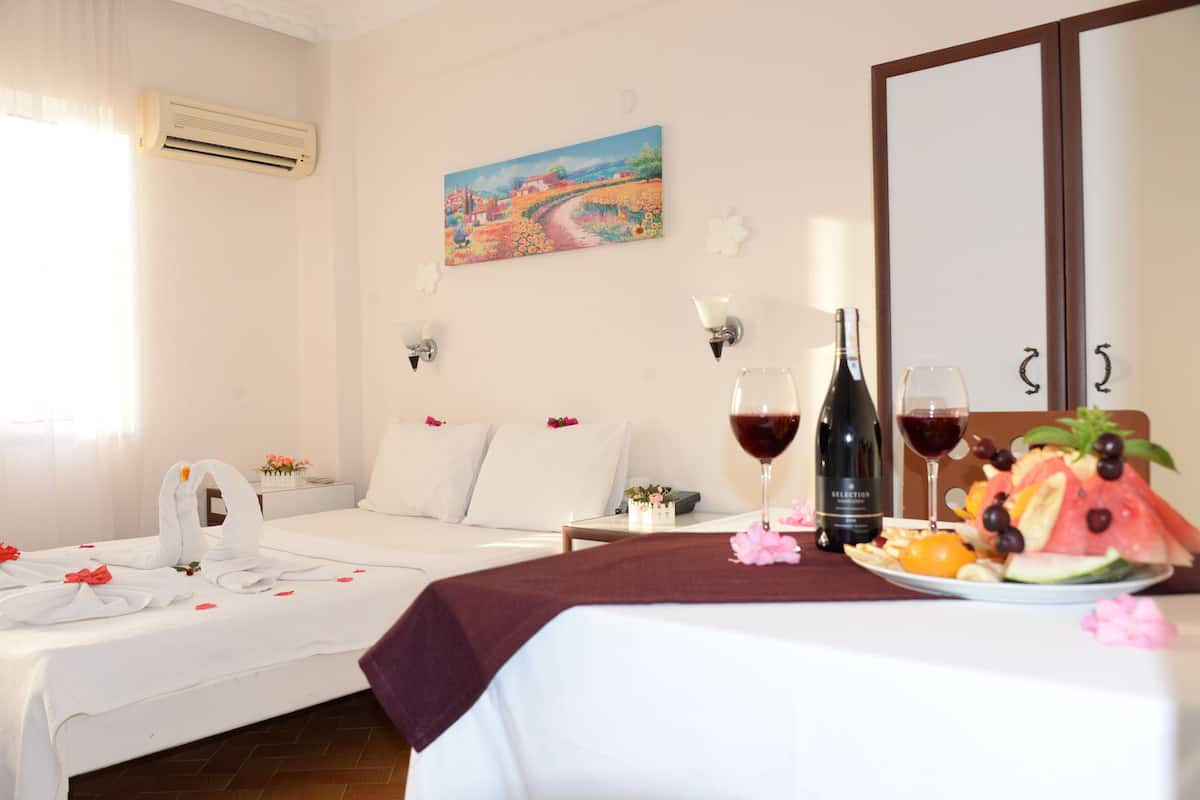 A hotel room with two beds, a painting on the wall, a bottle of wine, and a fruit plate on the nightstand.