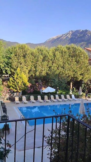 Una piscina con sillones de descanso y montañas al fondo.