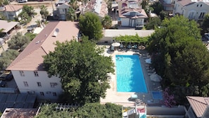 Vista aérea de una zona residencial con piscina rodeada de árboles y algunas casas.