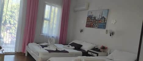 A hotel room with two beds, a painting of a cityscape, a window with pink curtains, and an air conditioning unit.