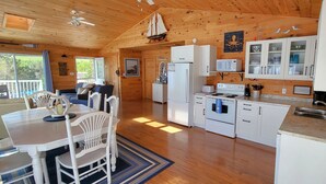 A cabin-style kitchen with wooden floors, white cabinetry, a refrigerator, stove, microwave, and a dining area with a table and chairs. - Water View Cottage With A/C In Quiet Location, Close To Amazing Beaches (Kensington)