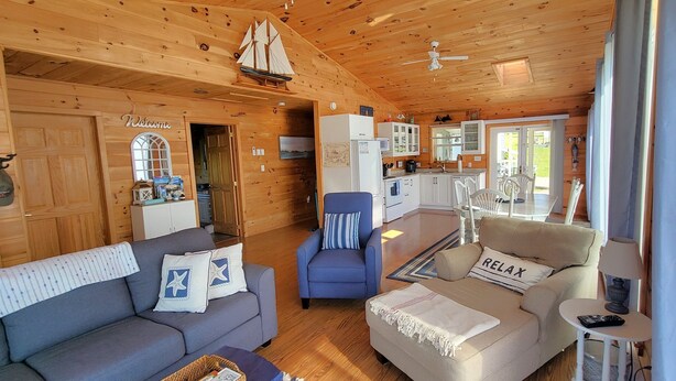 A cozy cabin interior with a wooden interior, a sofa, a chair, a small table, and a kitchenette. - Water View Cottage With A/C In Quiet Location, Close To Amazing Beaches (Kensington)