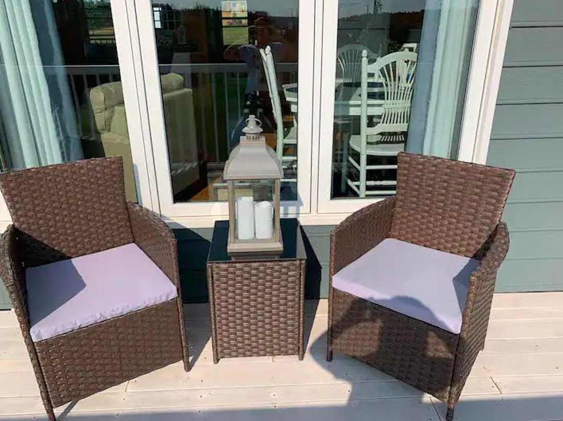 Deux fauteuils en osier avec des coussins, une petite table et une lanterne sur une terrasse en bois.