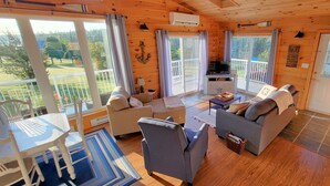 A cozy cabin with a living room, dining area, and a balcony with a TV. - Water View Cottage With A/C In Quiet Location, Close To Amazing Beaches (Kensington)