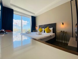 Quarto de hotel moderno com uma cama grande, uma escrivaninha e vista para a paisagem urbana.