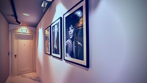 A hallway with framed pictures on the wall, a door at the end, and a marble floor. - Cinematique (Mosta)