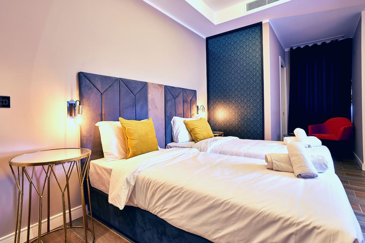 A hotel room with two beds, a round table, and a red chair.