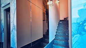 A marble staircase with a handrail, a light fixture, and a door at the top. - Cinematique (Mosta)